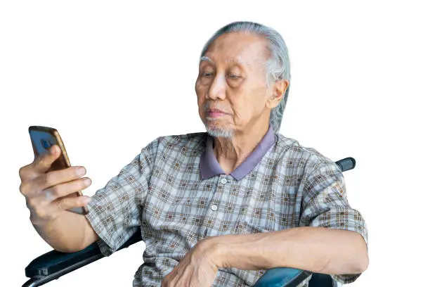 Picture of an elderly man reading a message on the smartphone while sitting in the wheelchair, isolated on white background