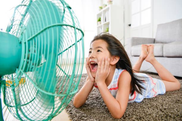 beautiful little kid girl lying down on floor beautiful young little kid girl lying down on floor at home and face to electric fan shouting to enjoy cooling breeze during summer season. selective focus photo. japan small apartment stock pictures, royalty-free photos & images