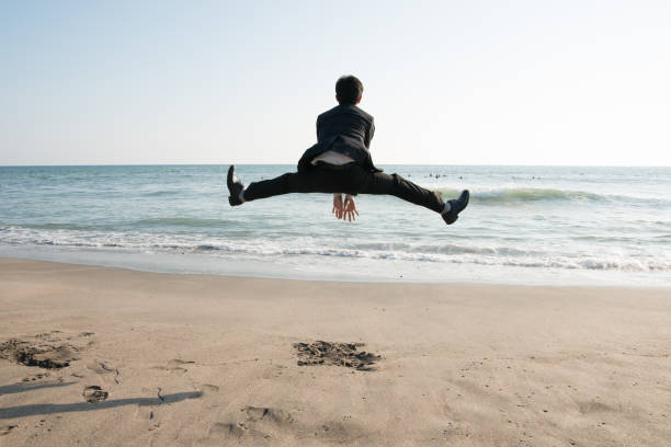 ビーチでビジネスマンをジャンプ: 日常生活からの脱出 - men businessman jumping levitation ストックフォトと画像