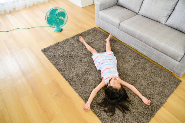 high angle view photo of girl lying down on carpet high angle view photo of lovely attractive little girl lying down on carpet sleeping resting and blowing electric fan enjoying cool wind during summer season. floor fan stock pictures, royalty-free photos & images