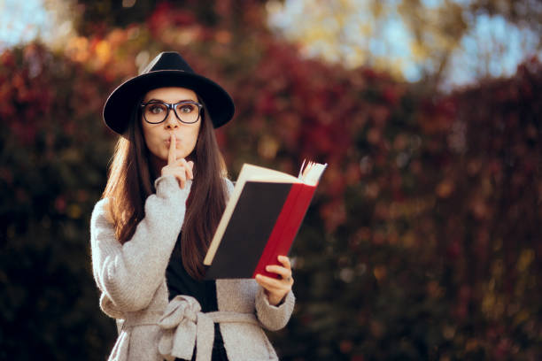 hipster estudante segurando um livro ao ar livre na decoração de outono - finger on lips whispering secrecy women - fotografias e filmes do acervo