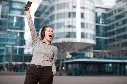 cheerful business woman in the city cheering her success, holding smart phone.