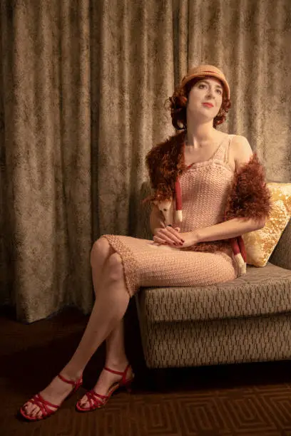 Young woman in 1920s flapper dress with fox fur and cloche sitting in a chair.