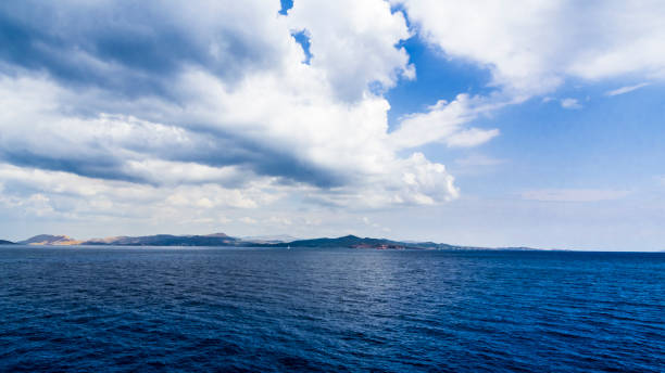 The mountainous coast of the Aegean sea is covered with storm clouds and the deep coastal waters are dark blue.