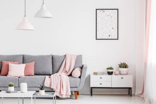 istock Poster above cabinet with plants in white flat interior with pink blanket on grey couch. Real photo 1014655772
