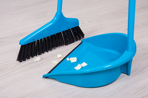 close up of broom and dustpan with paper trash on wooden floor