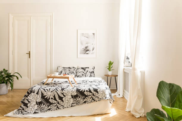 istock Comfortable big bed with white and black flower design bedding and a breakfast tray on in a wooden floor bright bedroom interior. Double door to another room in a background wall. Real photo. 1014658752