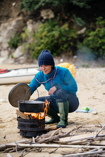 Woman cooking and preparing lunch on a beach after sea kayaking