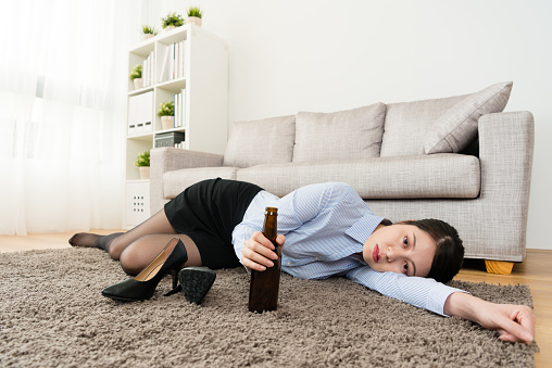 unhappy young female office worker lying down on living room floor resting when she losing work and back to home drinking beer.