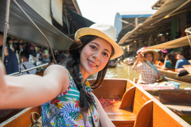 happy girl tourist taking self-portrait photo happy pretty girl tourist taking self-portrait photo selfie on boat when she visiting popular floating market during asia Thailand travel. ratchaburi province stock pictures, royalty-free photos & images