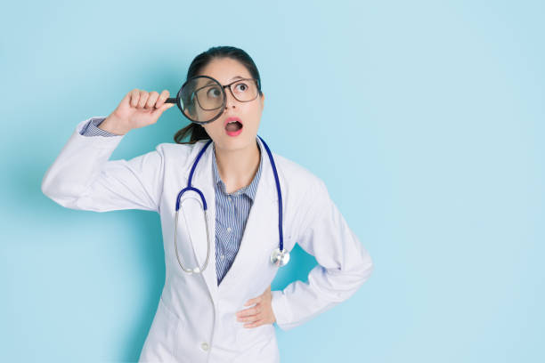 young female doctor standing in blue background attractive young female doctor standing in blue background using magnifier looking at air thinking care solution and having good idea feeling shocked. photographic enlarger stock pictures, royalty-free photos & images