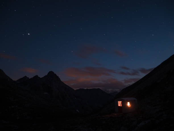 The Milky Way and the starry sky from high up on the Alps with scenic mountain landscape. People standing aside a little chapel with lightning gear on.