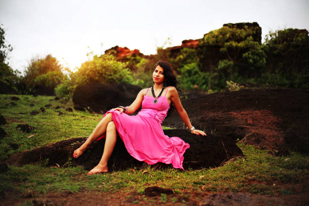 Young fashion girl sitting on a rock Young Indian fashion girl sitting on a rock near Chapora fort, Goa. She wearing pink color dress and looking to the camera. chapora fort stock pictures, royalty-free photos & images