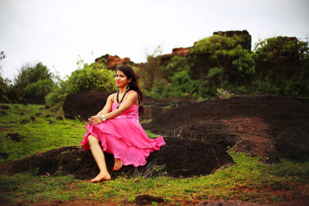 Young fashion girl sitting on a rock Young Indian fashion girl sitting on a rock near Chapora fort, Goa/India. She wearing pink color dress and looking to the camera. chapora fort stock pictures, royalty-free photos & images