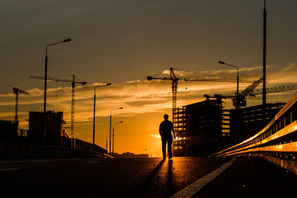 Silhouette of a man walking on a bridge at sunset.