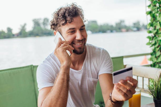 istock Smiling guy holding credit card when talking on mobile phone 1014732796