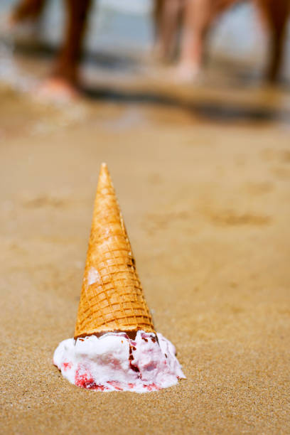 closeup of an ice cream cone upside down dropped on the sand of a beach