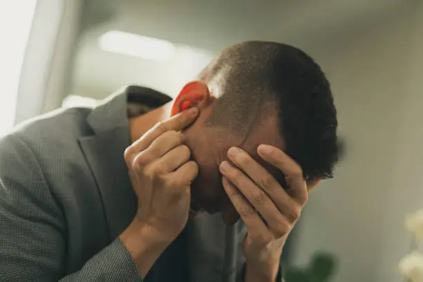 closeup of a suffering caucasian man with one hand in his head and the other hand covering his ear