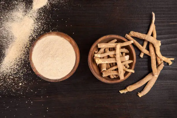 Roots and powder of Ashwagandha also known as Indian ginseng on wooden background, top view.