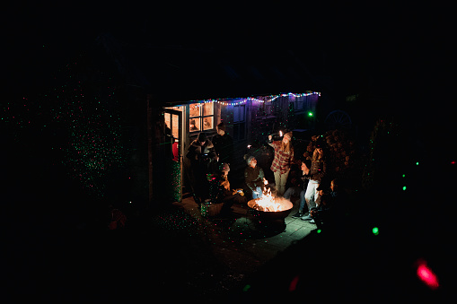 Small group of people are having a winter party in the garden with a bonfire and sparklers.