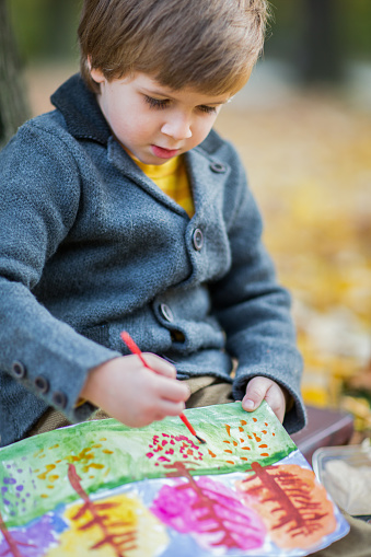Young talented artist boy paints a picture in the autumn forest.