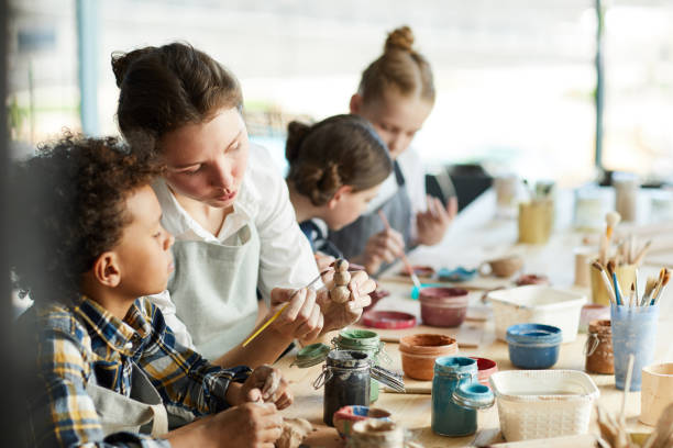 Advice of teacher Young teacher showing one of pupils clay item and giving advice about painting it art workshop stock pictures, royalty-free photos & images