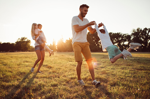 Young mother and father playing with their kids on a sunny summer day in the park