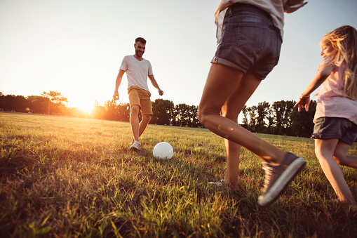 Young parents playing soccer with their daughter on a beautiful grass field at summer