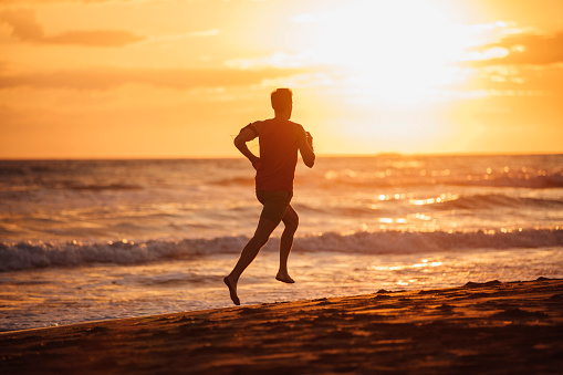 Man running at the beach looking at the breathtaking sunset over the horizon