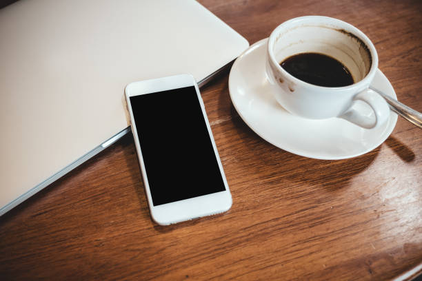 istock Top view mockup image of a white mobile phone with blank black desktop screen on a computer laptop with coffee cup 1014758702