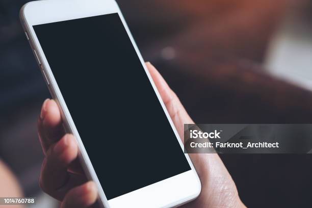 Mockup Image Of A Hand Holding White Mobile Phone With Blank Black Desktop Screen With Blur Background Stock Photo - Download Image Now