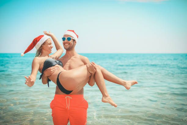 istock Young couple on the beach with Santa Claus caps 1014764236
