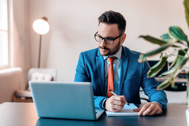 istock Handsome businessman in eyeglasses is making notes while working on a laptop. 1014770548