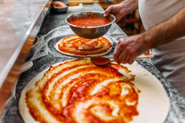istock Chef baker making pizza at the kitchen. Adding tomato sauce on a pizza dough. 1014771168