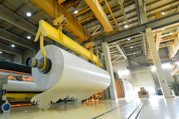 Photo of large roll of paper on a crane in a mill for the production of paper for further processing in a printing plant - recycling of waste paper