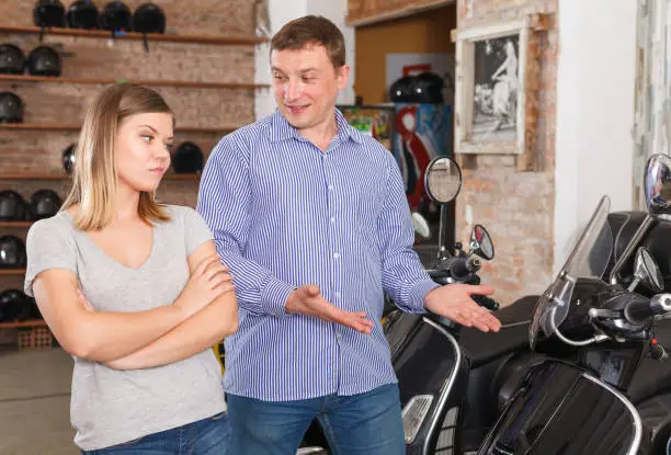 Couple is talking about new motobikes and female is surprised choice man in the moto store.