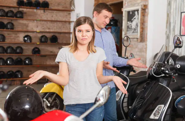 Couple is talking about new motobikes and female is surprised choice man in the moto store.