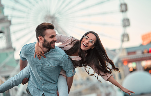 Love is in the air! Cute romantic couple spending time together in the city. Handsome bearded man and attractive young woman are in love. Hugging, kissing and having fun on the Ferris wheel background.