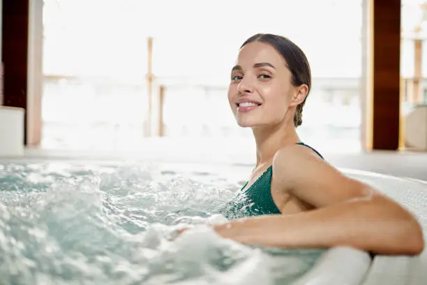 Young woman relaxing in soft waving water while sitting in hot tub bath at spa center