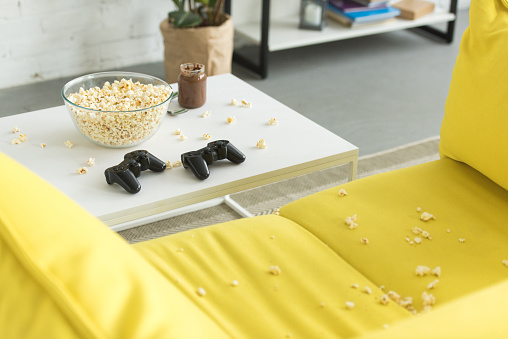 glass bowl with popcorn and joysticks on table, yellow sofa in living room
