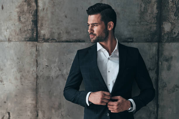 Charming man. Handsome young man in suit looking away and adjusting his jacket while standing indoors modelang stock pictures, royalty-free photos & images
