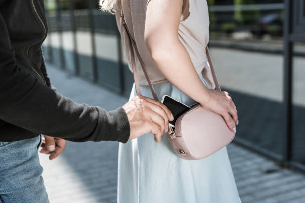 cropped view of criminal man pickpocketing smartphone from womans bag on street stock photo