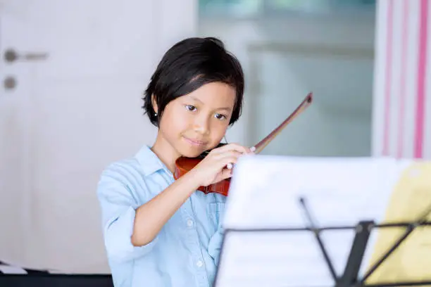 Picture of a little girl looking at paper notes while practicing and playing violin at home