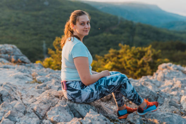 donna con diabete seduta in cima alla collina e che indossa una pompa di insulina - ponytail brown hair tourist women foto e immagini stock