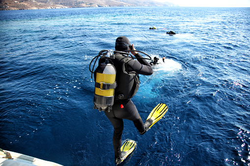 Group of scuba divers fully equipped with gear jumping into the water and preparing for diving