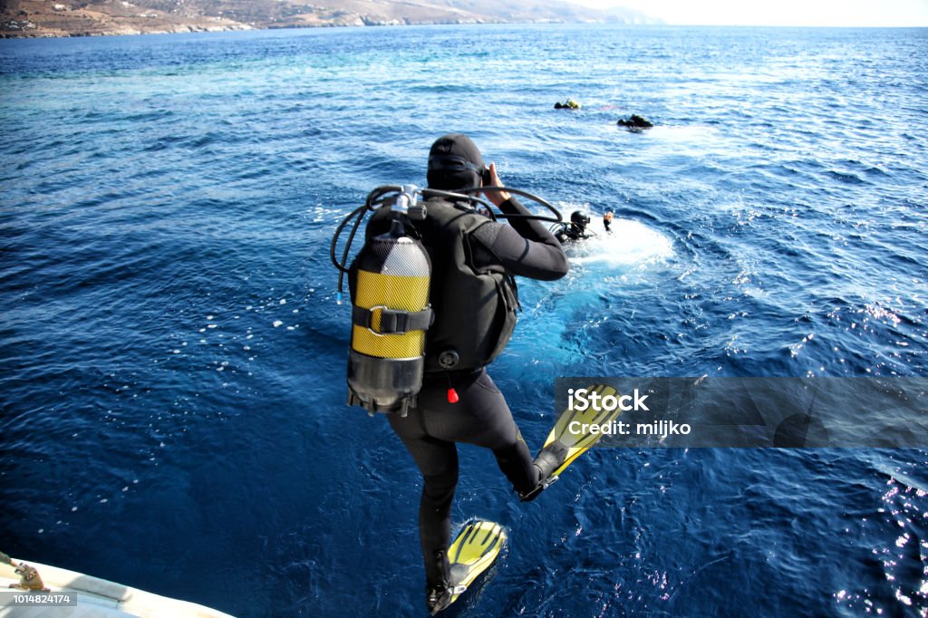 Divers jumping from the boat in water Group of scuba divers fully equipped with gear jumping into the water and preparing for diving Scuba Diving Stock Photo