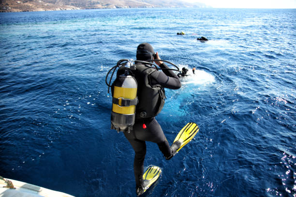 Divers jumping from the boat in water Group of scuba divers fully equipped with gear jumping into the water and preparing for diving diving into water stock pictures, royalty-free photos & images