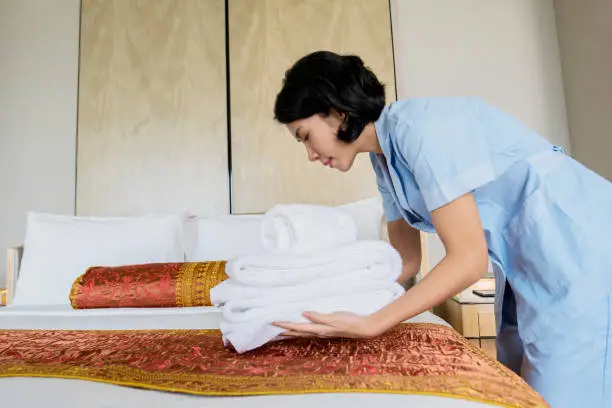 Image of female maid putting a pile of clean towels on the bed sheet. Shot in the hotel