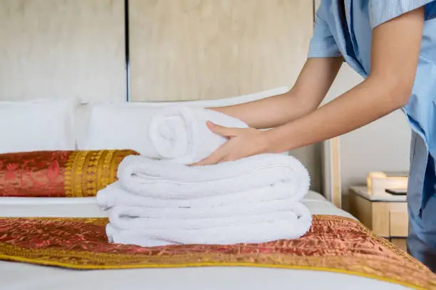 Closeup of young female maid hands tidying a stack of white bath towels on the bed sheet