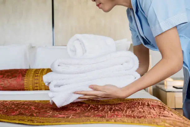Picture of unknown female maid putting a stack of white bath towels on the bed sheet
